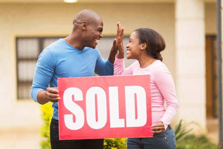 cheerful young african couple holding sold sign and celebrating their house been sold